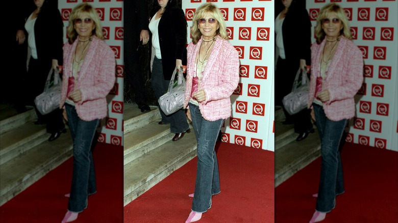 Nancy Sinatra posing on a red carpet wearing dark jeans with a pink blazer and pink shoes.