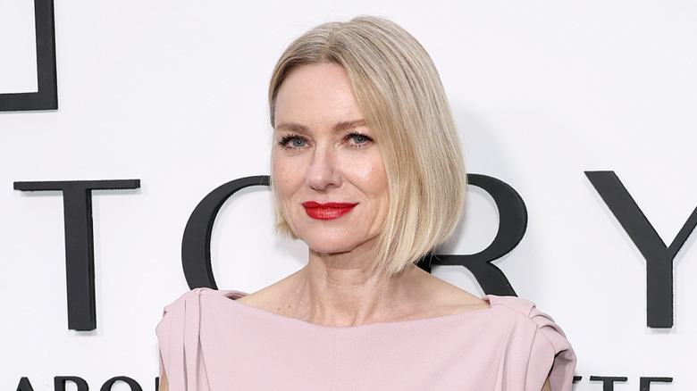 Naomi Watts posing at a red carpet event, wearing a pink top and a bright red lip.