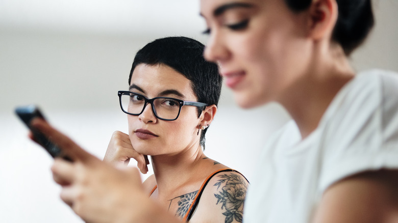 Unhappy woman watching partner on phone