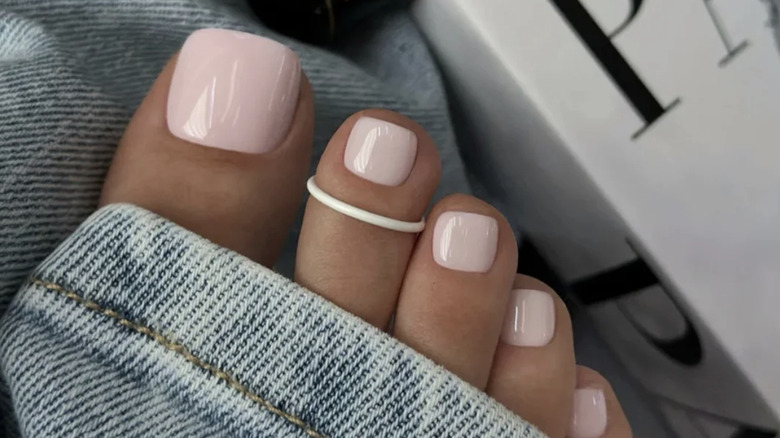 Baby pink pedicure with a white toe ring on the second toe