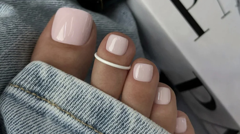 Baby pink pedicure with a white toe ring on the second toe.