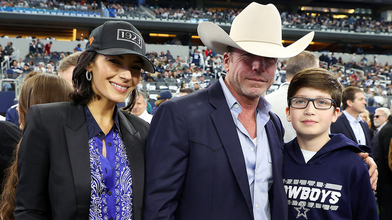 Nicole, Taylor, and Gus Sheridan pose together at a sporting event with crowds in the background.