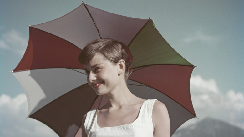 Audrey Hepburn smiling beneath a colorful umbrella