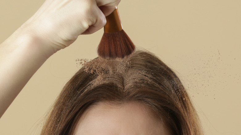 Person dabbing brunette dry shampoo on hair with brush