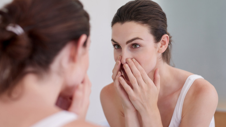 woman examining face in mirror