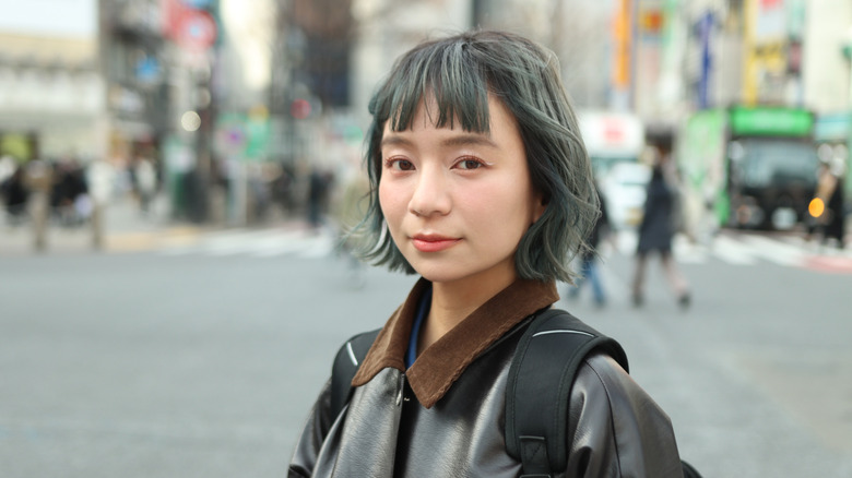 Woman walking through a city wearing a black leather jacket and a lived in, gray bob.