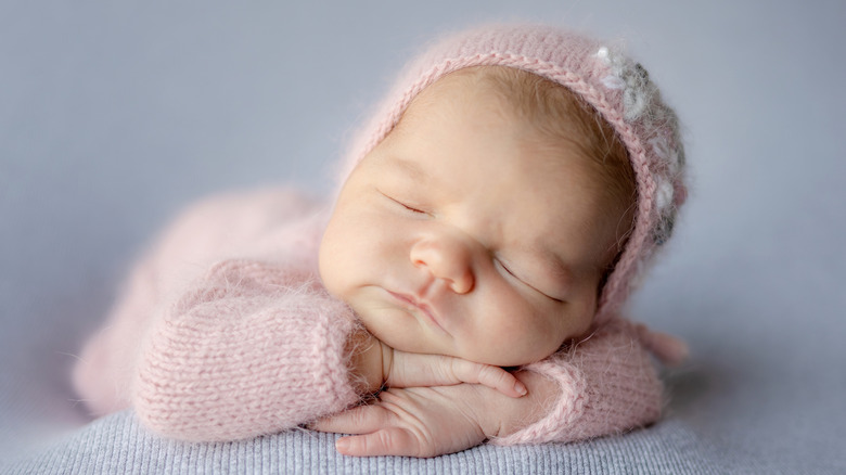 A newborn baby sleeping in a pink outfit and bonnet