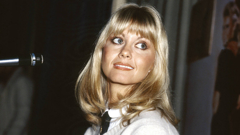 Olivia Newton-John looks over her shoulder while wearing dark eyeliner and a warm auburn lipstick.