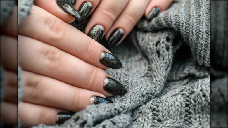 A half-moon manicure with dark glitter nailpolish.
