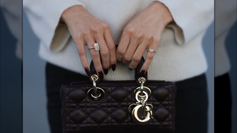 A woman with dark wine-red nails holding a purse.
