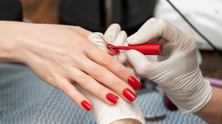 A woman getting her nails painted red.
