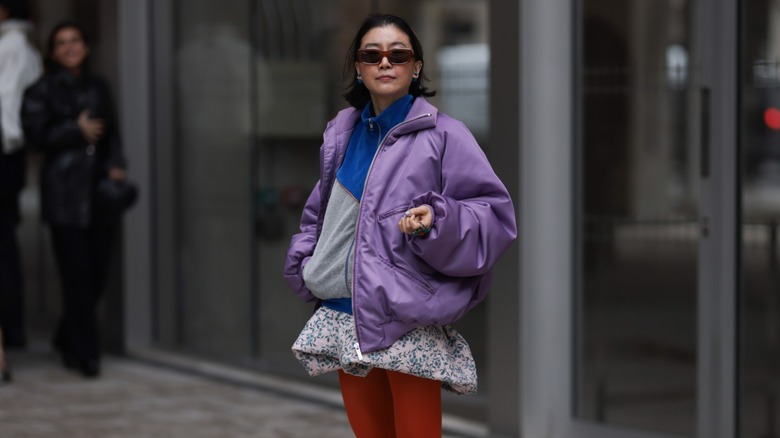 A woman wearing a violet bomber jacket, a pink floral bubble skirt, and red tights.