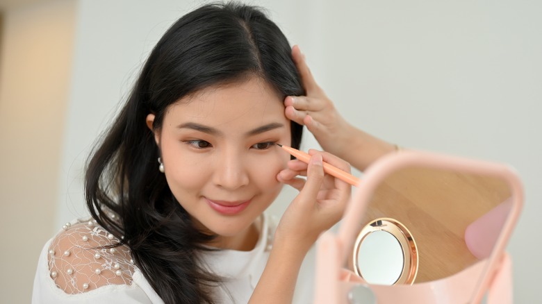 Asian woman applying eyeliner