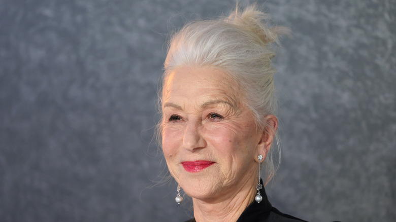 Helen Mirren posing against a gray background wearing drop earrings with her hair up.