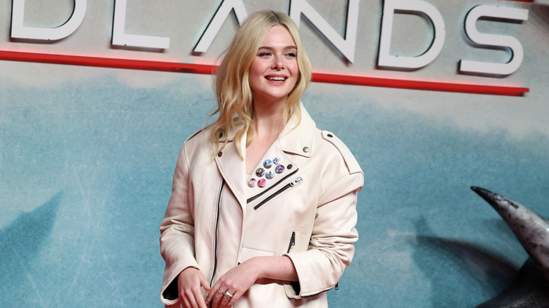 Elle Fanning smiling in an off-white jacket