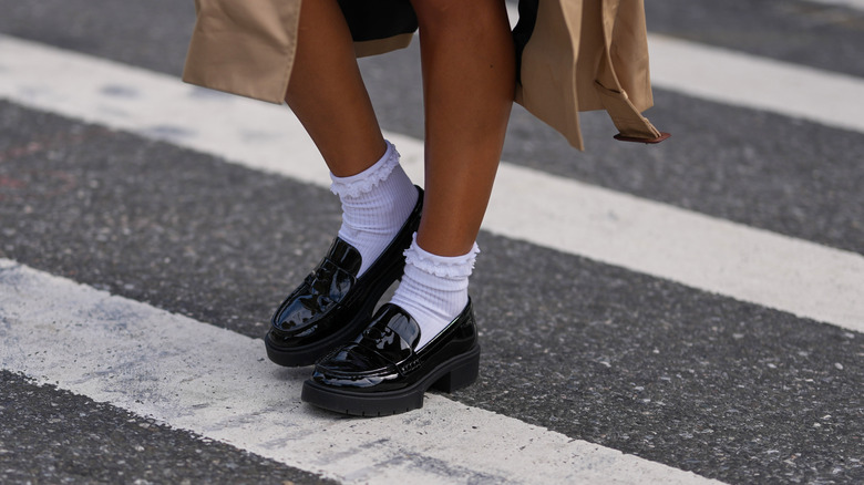 A woman wearing lug-sole loafers and a trench coat.