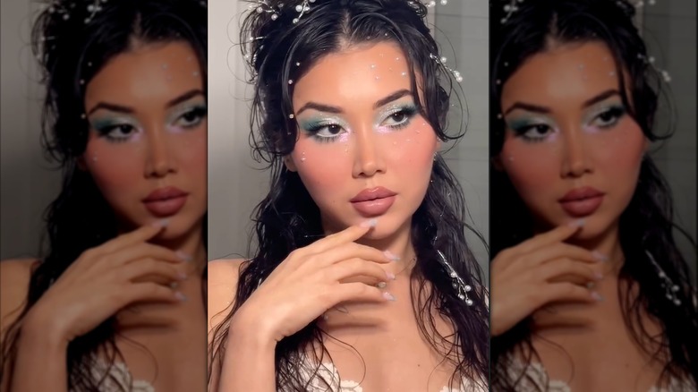A woman wearing mermaidcore makeup, featuring blue-green eyeshadow and sun-kissed blush