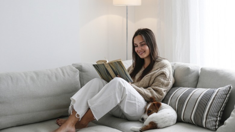 A woman reads on the couch with her dog