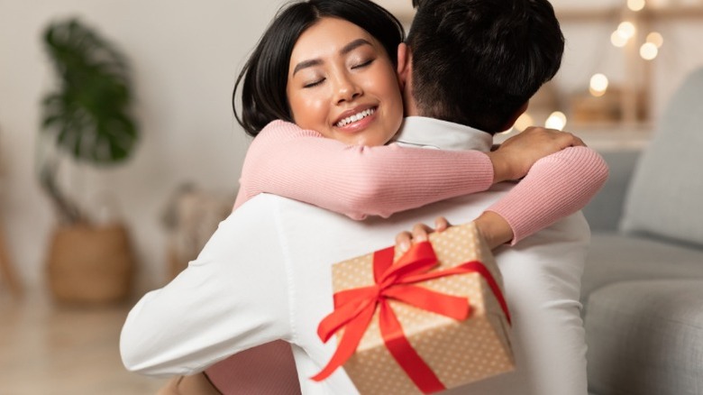 A woman holds a present as she hugs a man