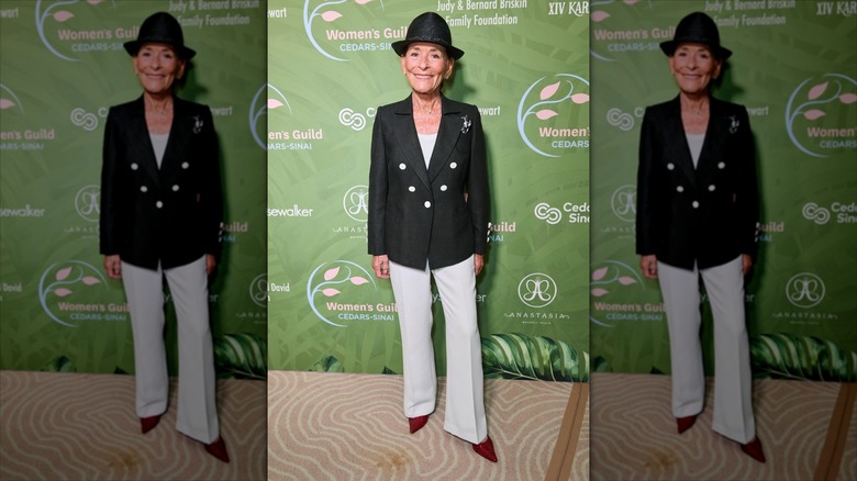 Judy Sheindlin wearing a black fedora hat with a black-and-cream pantsuit.