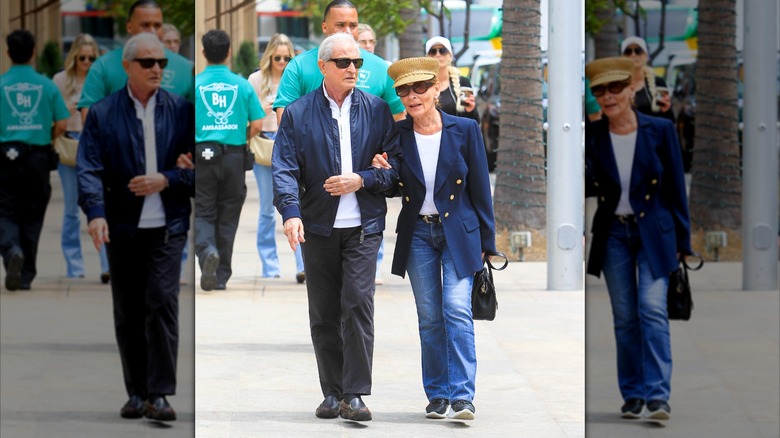Judy Sheindlin walks with her husband (L) wearing flared jeans and a white long-sleeve with a blue blazer and fishermans hat
