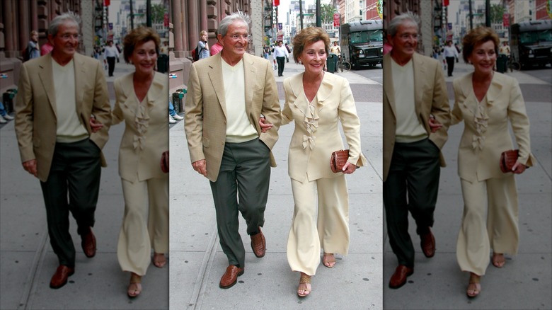 Judy Sheindlin walks with her husband (L) wearing wide-leg trousers and a ruffled blouse