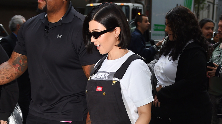 Kourtney Kardashian wearing a graphic tee and black overalls while pregnant