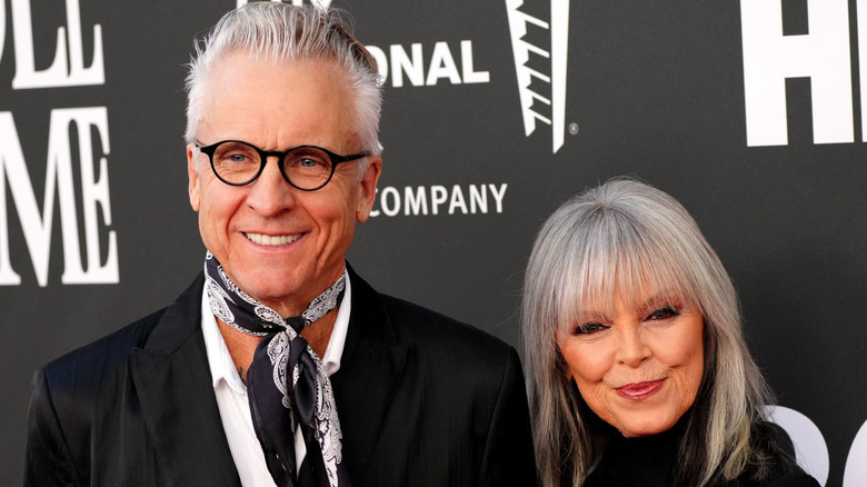 Pat Benatar and Neil Giraldo pose for a photo in front of a black and white back drop.