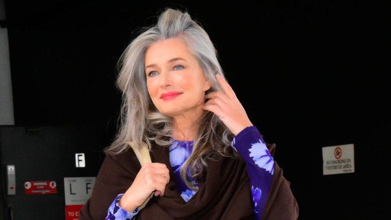 Paulina Porizkova wore her gray hair down with a bold lip and black eye liner along with a long brown sweater over her bright blue dress while arriving at "The Drew Barrymore Show" in March 2025 in New York City.