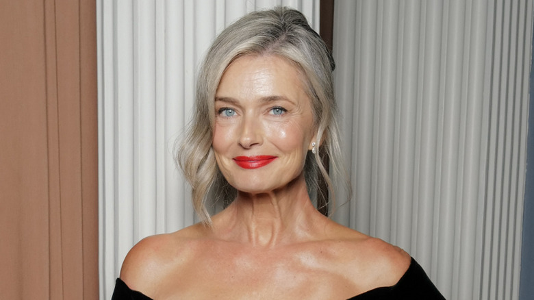 Paulina Porizkova posing at an event wearing an off-the-shoulder black dress and red lipstick with her hair in an updo.