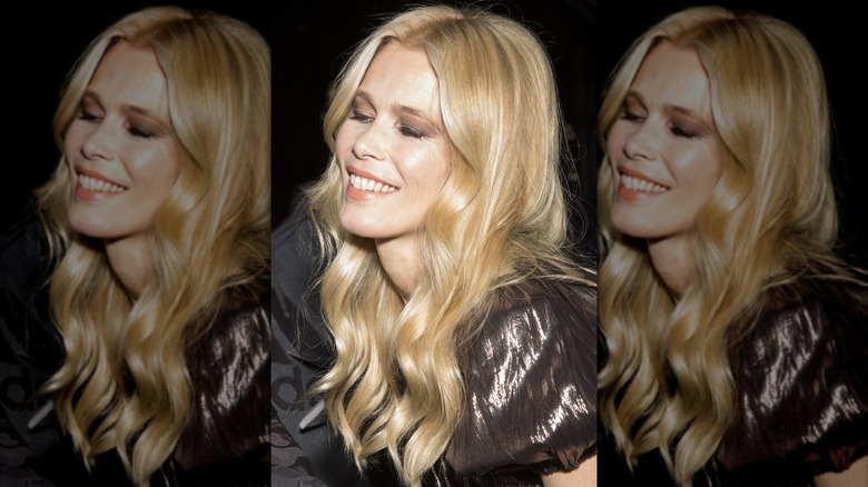Claudia Schiffer smiling with her eyes closed in a shiny metallic top and her curly hair down.