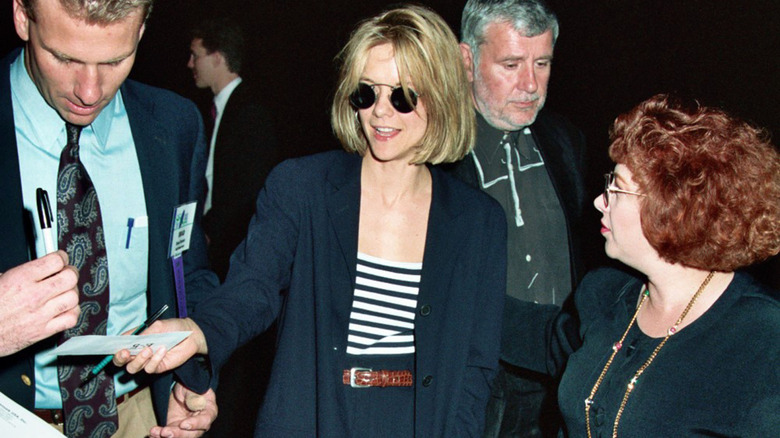 Meg Ryan pictured wearing a navy pantsuit with a striped shirt and sunglasses.