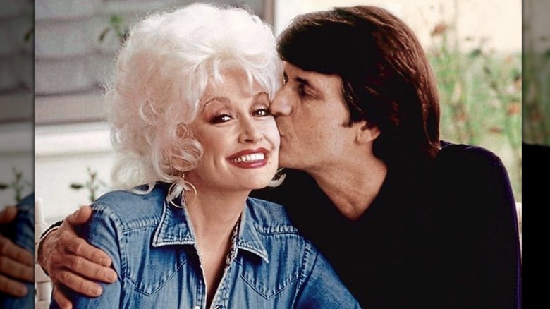 Dolly Parton smiles while husband Carl Dean plants a kiss on her cheek