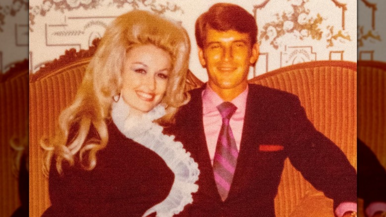 Dolly Parton and husband Carl Dean pose together while sitting on a retro orange couch