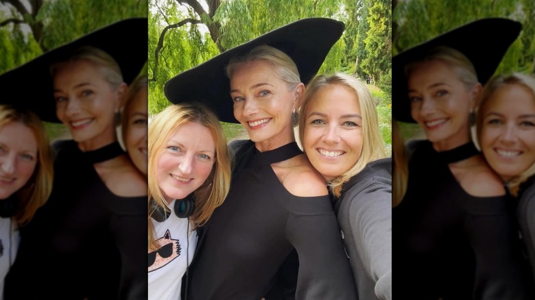 Paulina Porizkova posing outside next to two blonde women for a selfie in a black dress and flat hat.