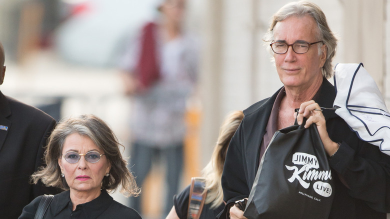 Roseanne Barr is walking next to partner Johnny Argent with a stern look on her face