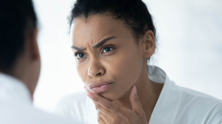 frowning Black woman looking into mirror