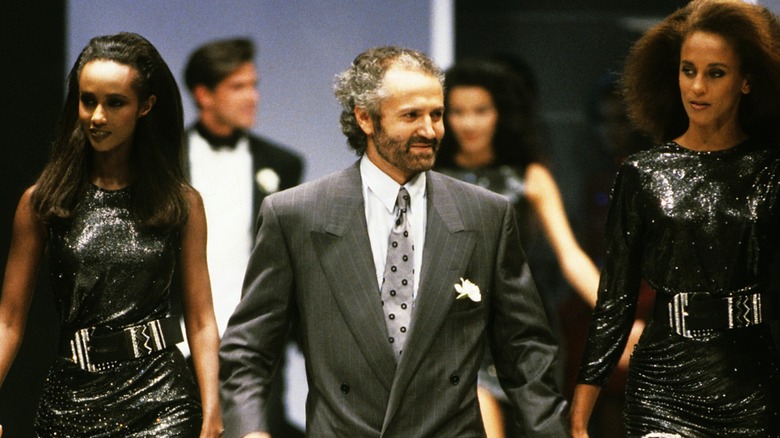 Gianni Versace presenting his collection in 1987 next to two models