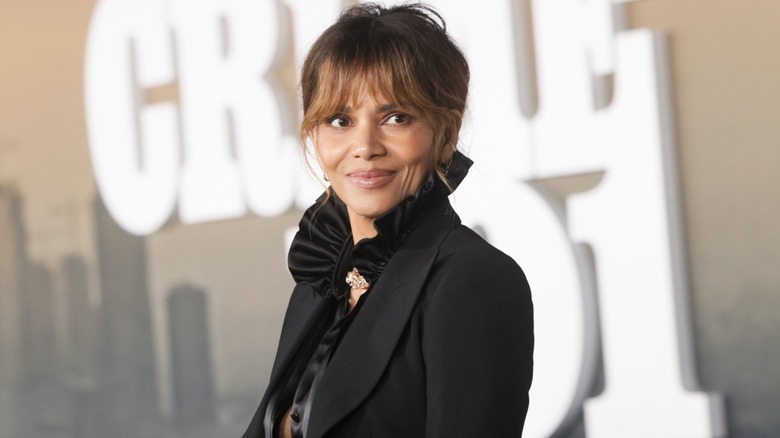 Halle Berry at an event with her hair up wearing a black jacket and black blouse with a ruffled neckline.