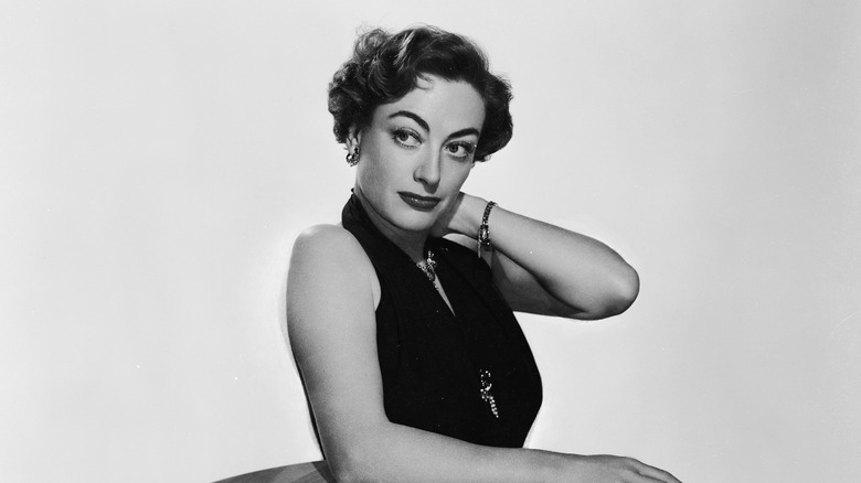 Joan Crawford leans on a table as she poses for a publicity still.