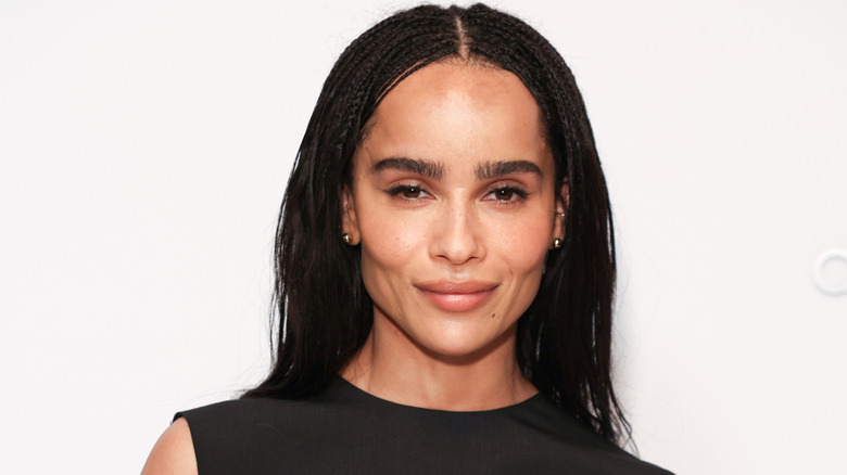 Zoë Kravitz flashes a soft smile to the camera while posing on the red carpet in a black dress.