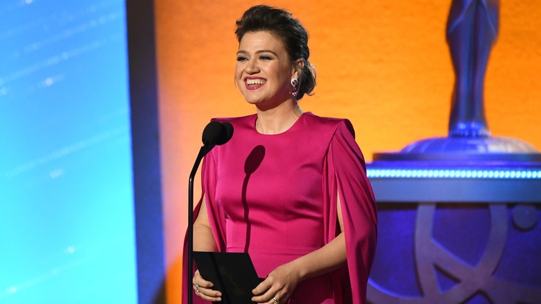 Kelly Clarkson presenting an award at the 2024 Emmys wearing a dark-pink gown.