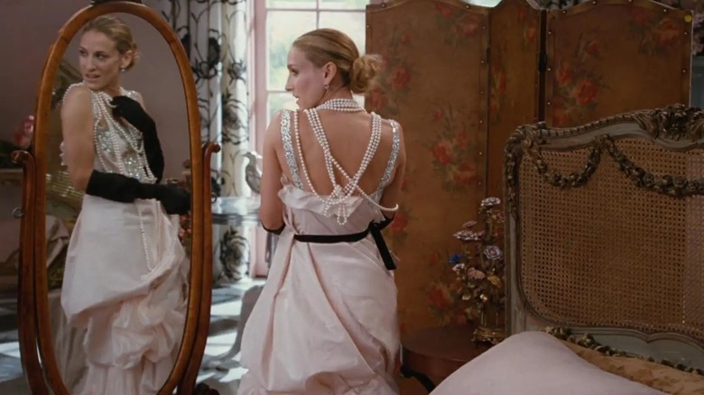 Sarah Jessica Parker as Carrie Bradshaw wearing a draped wedding dress with black gloves and pearl necklaces.