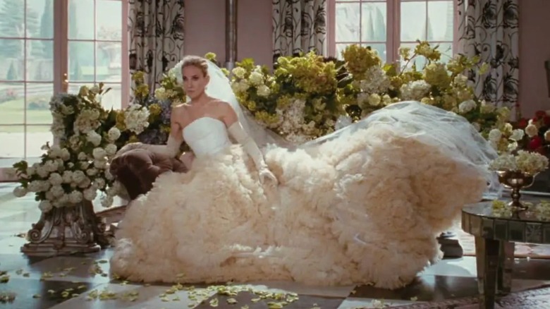 Sarah Jessica Parker as Carrie Bradshaw sitting down wearing a statement ballgown wedding dress and gloves.
