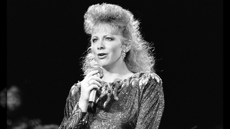 Reba McEntire wearing a sparkly top with teased-up hair performing in 1988.
