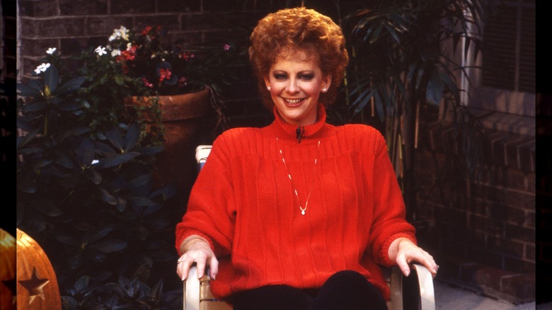 Reba McEntire wearing a bulky red sweater with a short voluminous hairstyle in 1987.