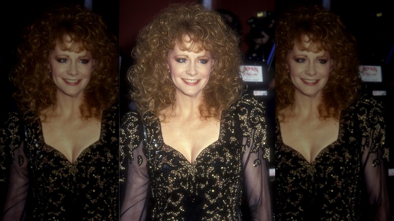 Reba McEntire wearing a black-and-gold dress with sheer sleeves with voluminous hair at the 1991 Academy Awards.