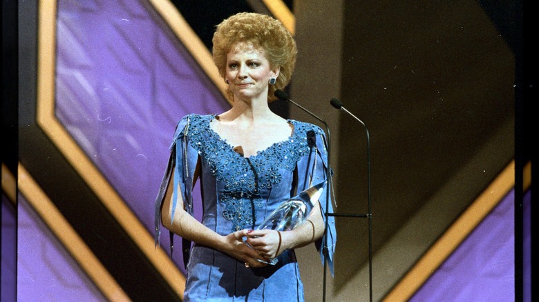Reba McEntire with a short, voluminous hairstyle wearing a blue dress on stage at the Country Music Association Awards in 1986.