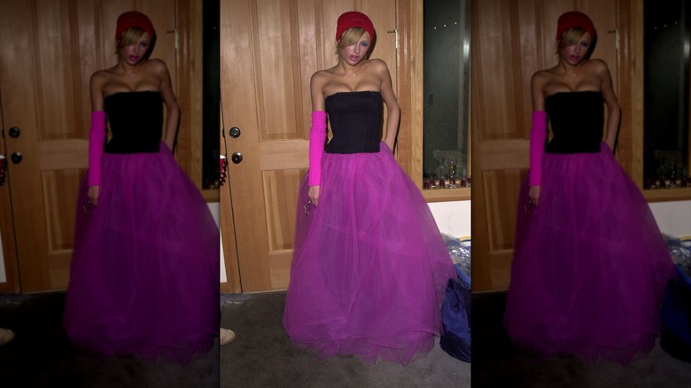 Paris hIlton posing in a beanie, arm warmer, pink skirt, and black bustier.