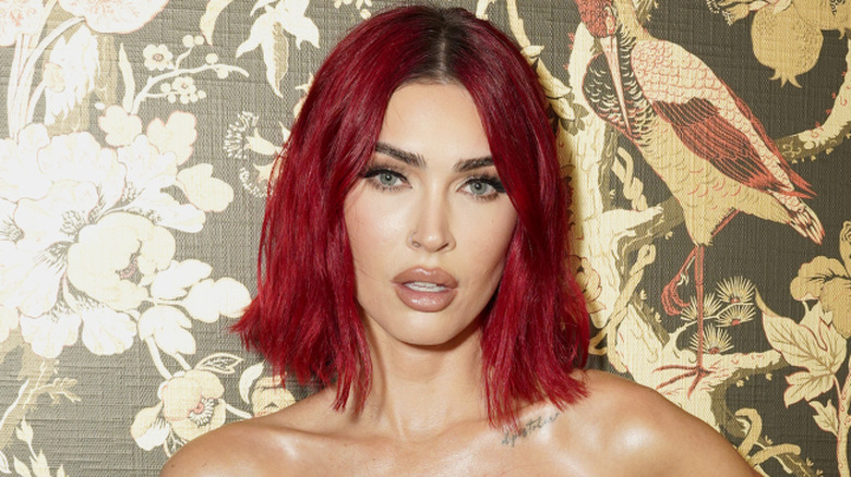 Megan Fox with bright red hair poses for a photo in a gorgeous white dress